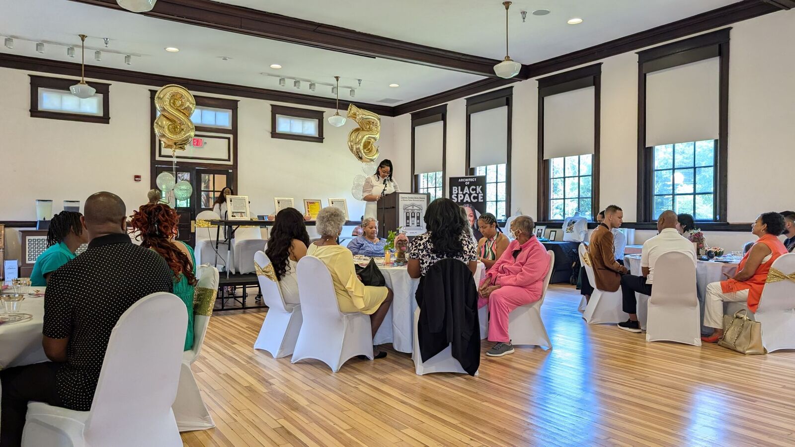 Neighbors seated at round tables in a bright community hall during a Juneteenth gathering